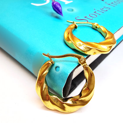 Twisted gold hoop earrings styled on a book for flatlay look