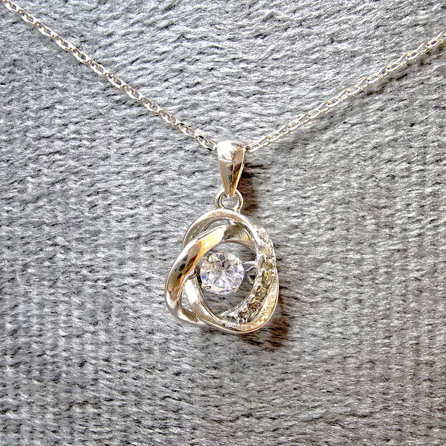 Round dancing stone pendant necklace with constant sparkle on a grey velvet display.