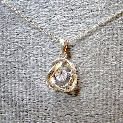 Round dancing stone pendant necklace with constant sparkle on a grey velvet display.