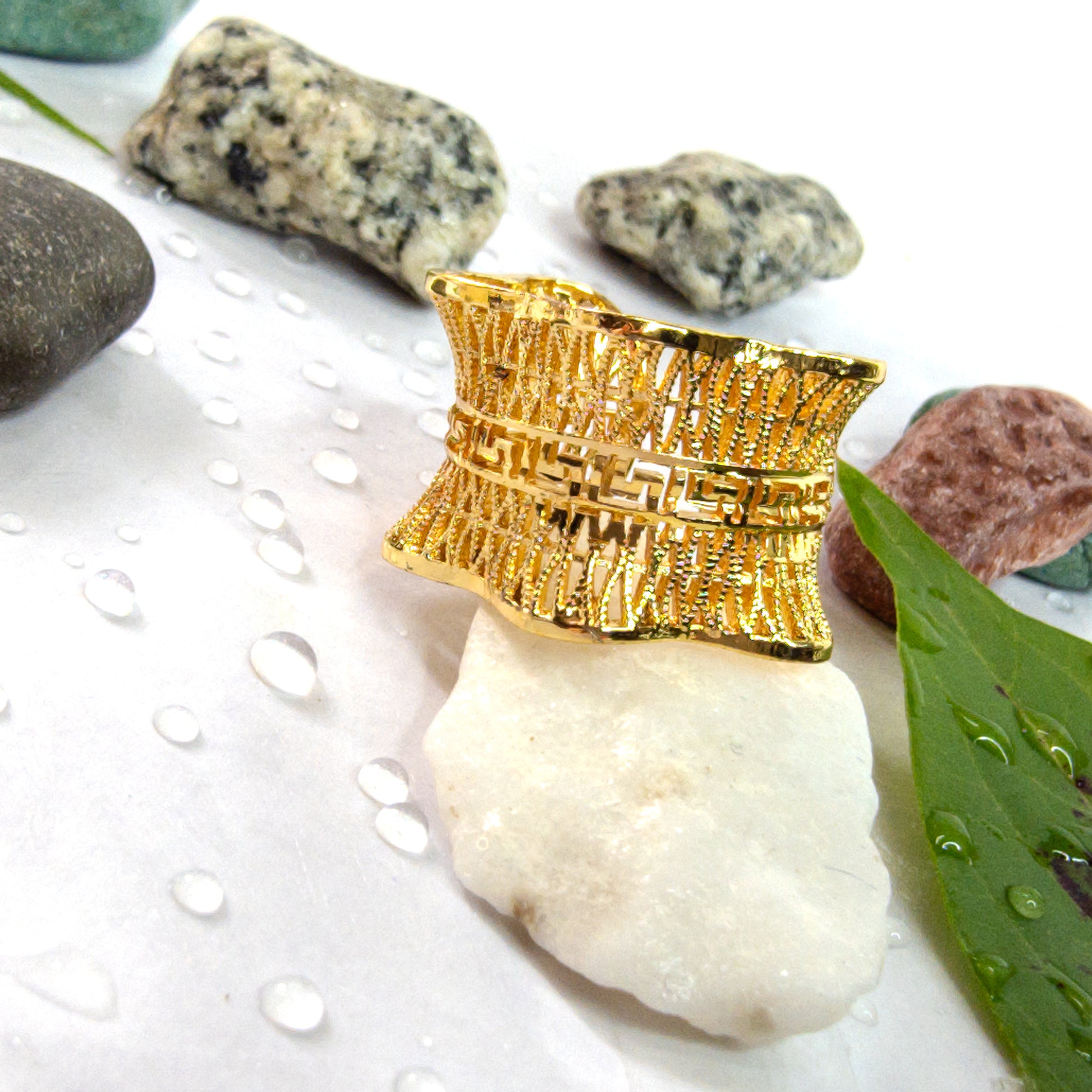 Close-up of the Empress Mesh Ring placed on a stone with droplets and leaves, emphasizing its texture.