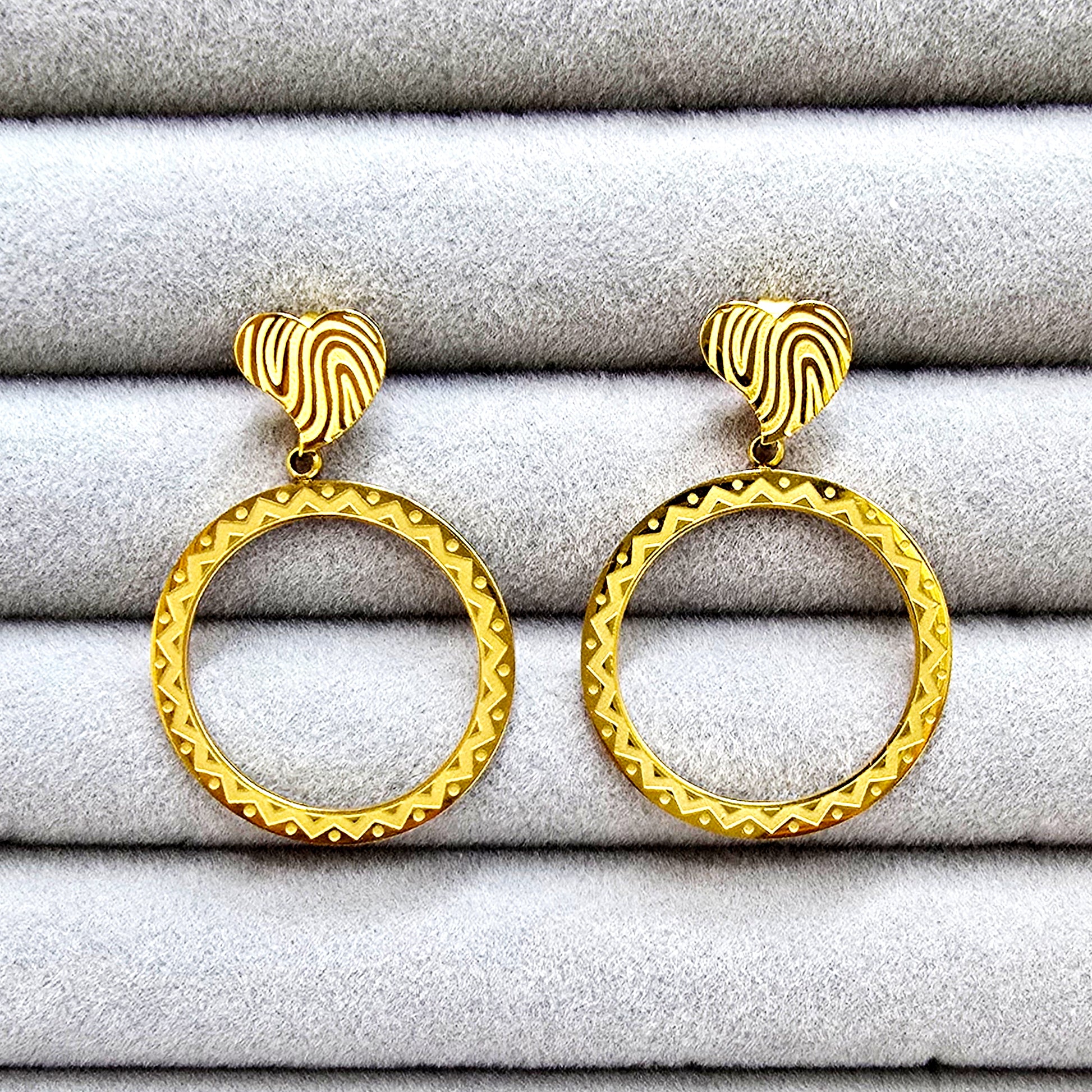 Close-up of a pair of gold etched heart drop earrings placed inside a grey velvet jewelry organizer tray.