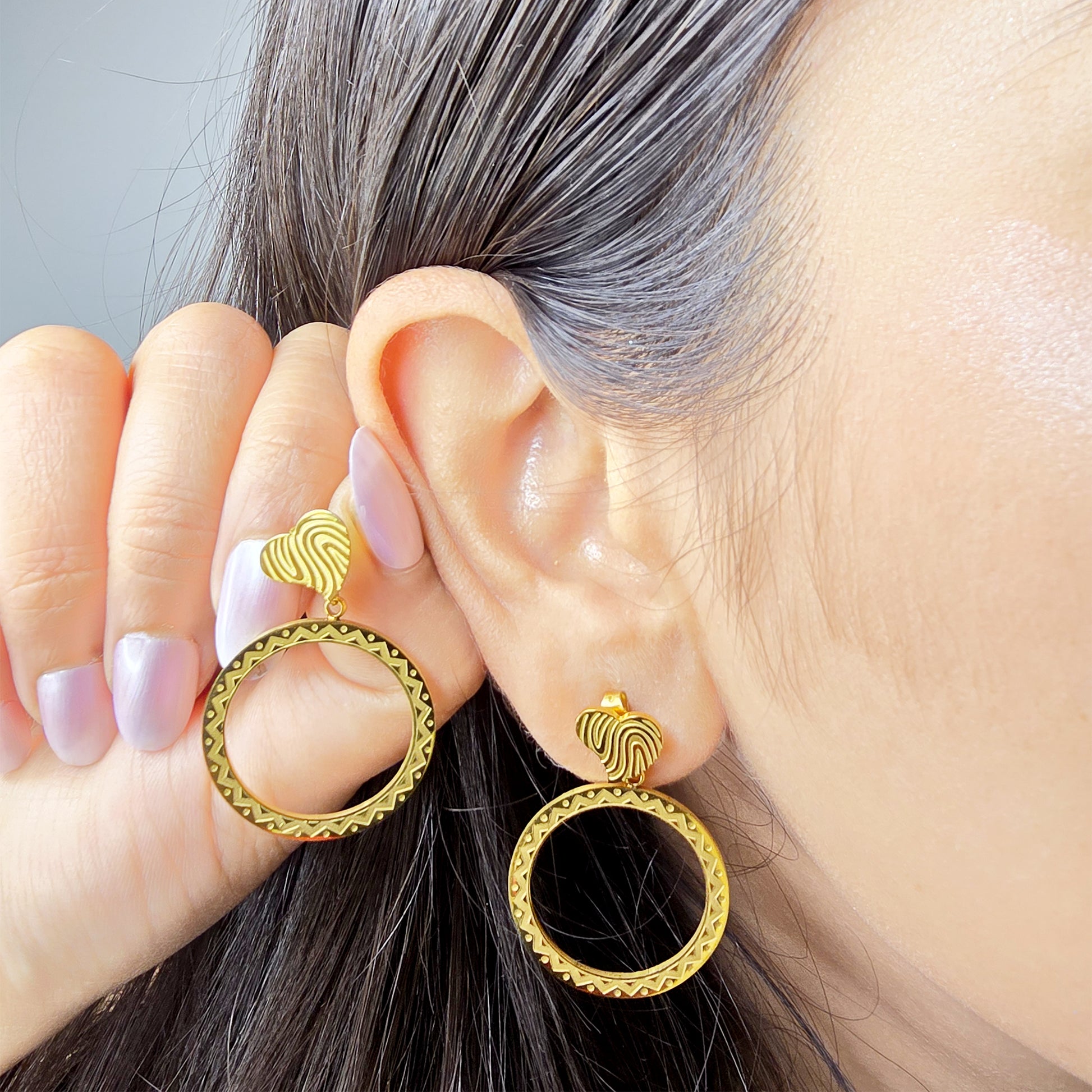 A model wearing the full drop etched heart earrings, highlighting the scale and high-shine gold finish against the skin.