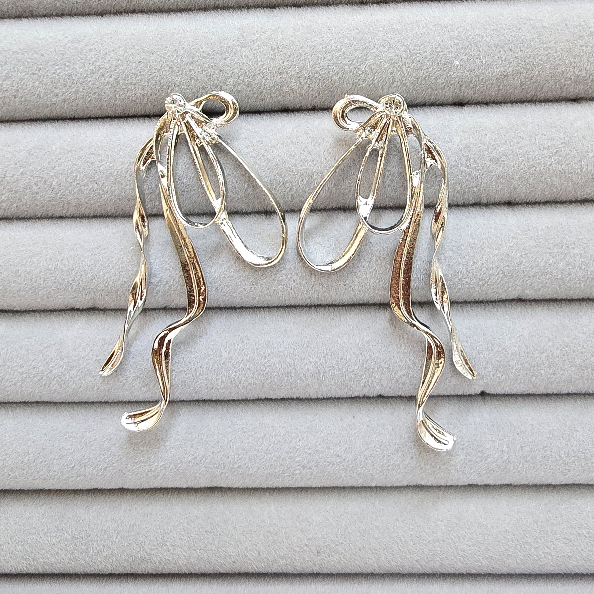 A pair of silver exaggerated bow earrings with wavy dangles displayed in a grey velvet jewelry organizer.