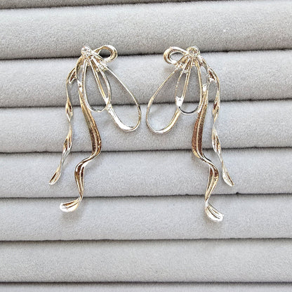 A pair of silver exaggerated bow earrings with wavy dangles displayed in a grey velvet jewelry organizer.