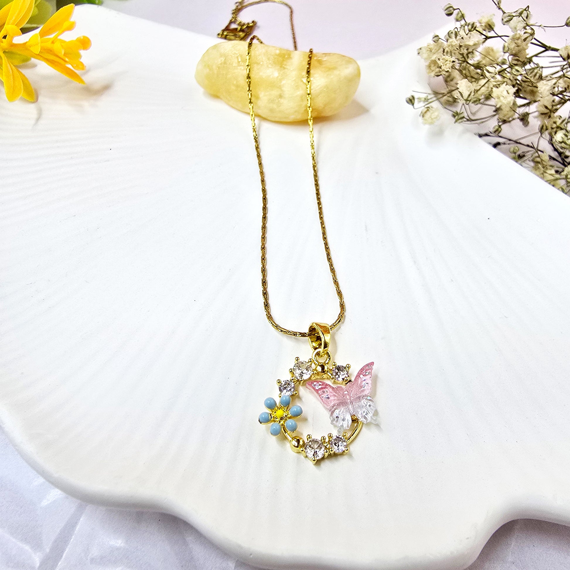 Gold-plated necklace featuring a pink enamel butterfly and blue forget-me-not flowers on a white surface.