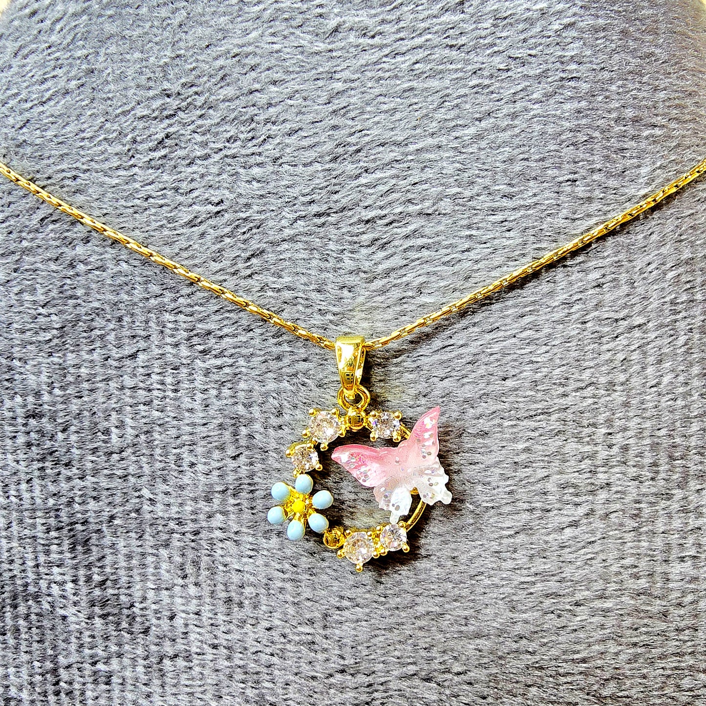 Close-up of crystal and enamel butterfly and flower pendant necklace on a grey textured display.