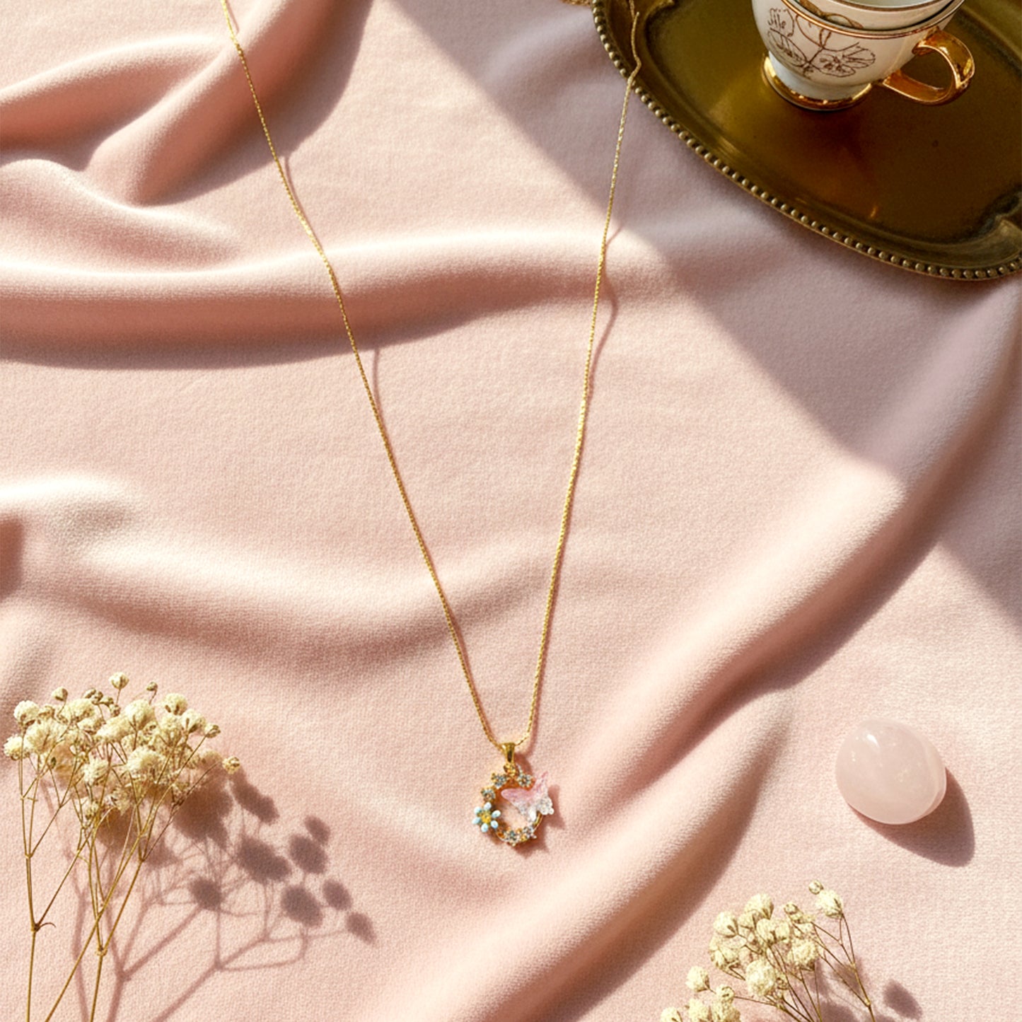 Whimsical butterfly and forget-me-not necklace styled on a soft pink velvet background in sunlight.