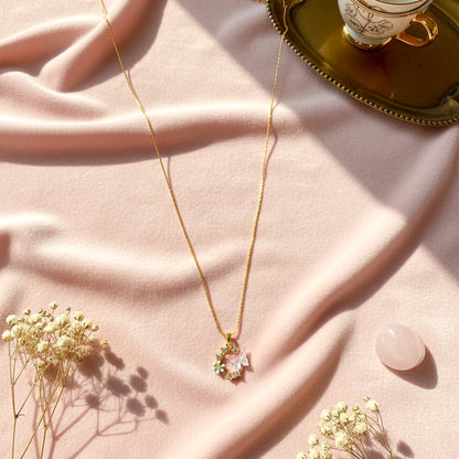Whimsical butterfly and forget-me-not necklace styled on a soft pink velvet background in sunlight.