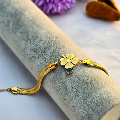 Close-up of gold herringbone chain and lucky clover charm with evil eye hanging detail.
