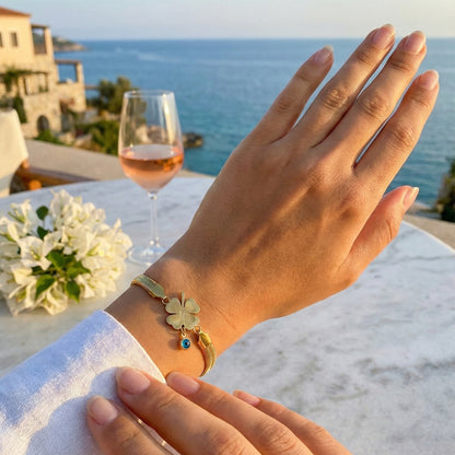 Woman's hand wearing gold snake chain clover bracelet with sea view background.