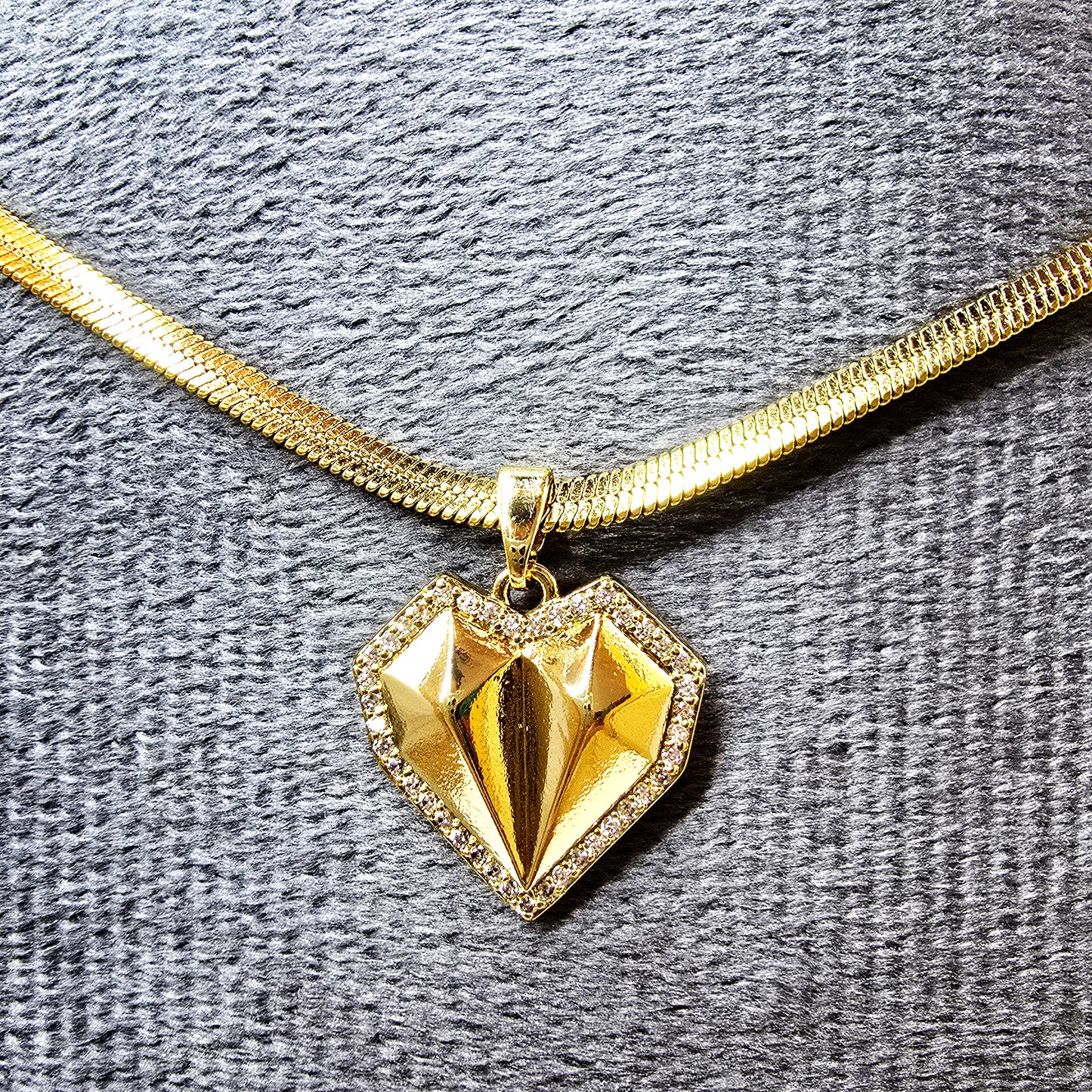Close-up of the geometric heart pendant showing the faceted gold center and crystal border on a grey display.