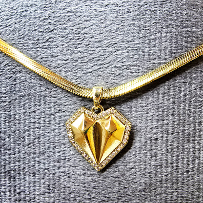 Close-up of the geometric heart pendant showing the faceted gold center and crystal border on a grey display.