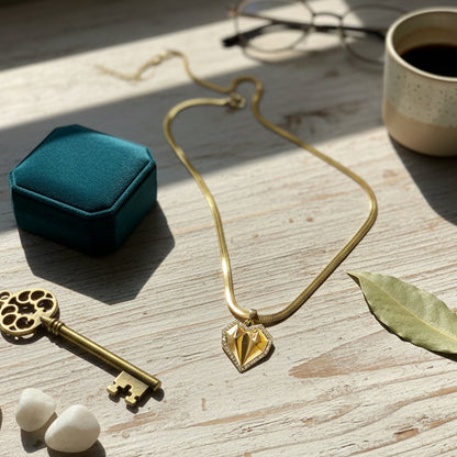 Geometric heart necklace with herringbone chain styled on a light wooden table with coffee and vintage key.