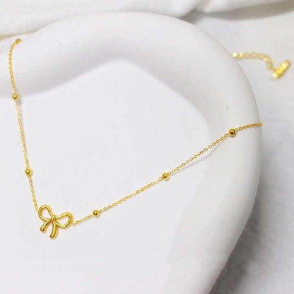 Gold-toned minimalist bow necklace styled on a curved ceramic surface for a soft, luxurious visual appeal.