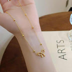 Gold bow necklace draped over a wrist, highlighting the bead detailing and fine craftsmanship