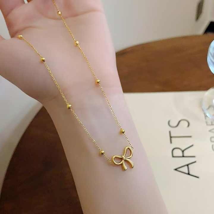 Gold bow necklace draped over a wrist, highlighting the bead detailing and fine craftsmanship