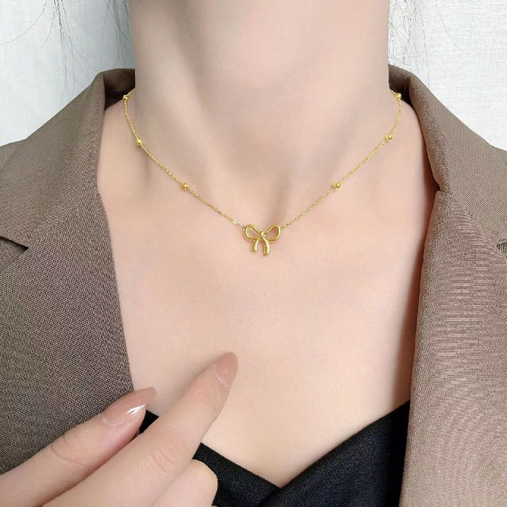 Minimalist gold bow necklace styled with a formal brown blazer, perfect for a chic office look.