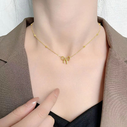 Minimalist gold bow necklace styled with a formal brown blazer, perfect for a chic office look.