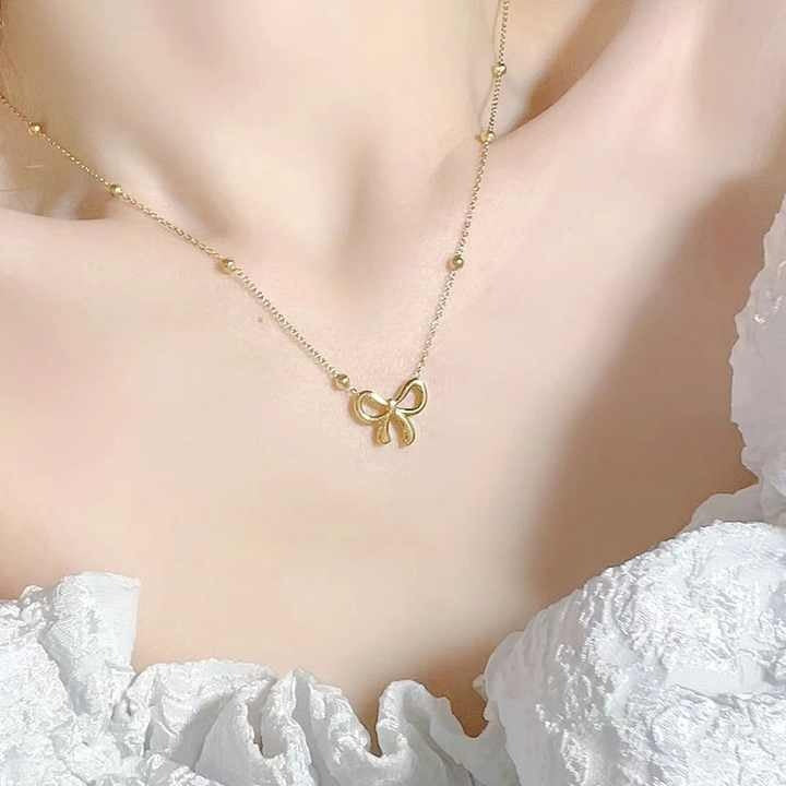 Gold bow pendant necklace worn with a white off-shoulder dress, showcasing its elegant and feminine look.