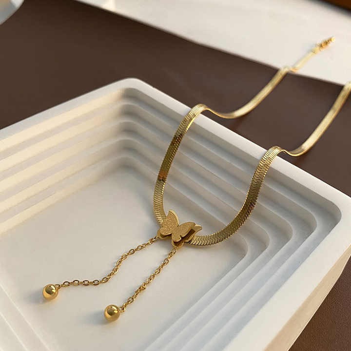 Gold-toned butterfly necklace with snake chain and dual drop chains on a white tray