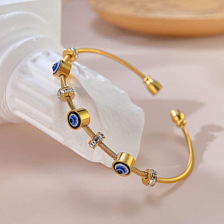 Angled view of an evil eye gold bangle resting on a glass jar, highlighting its sparkle and finish.