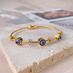 Devil’s eye gold wire bracelet with alternating crystal and evil eye beads displayed on textured stone.