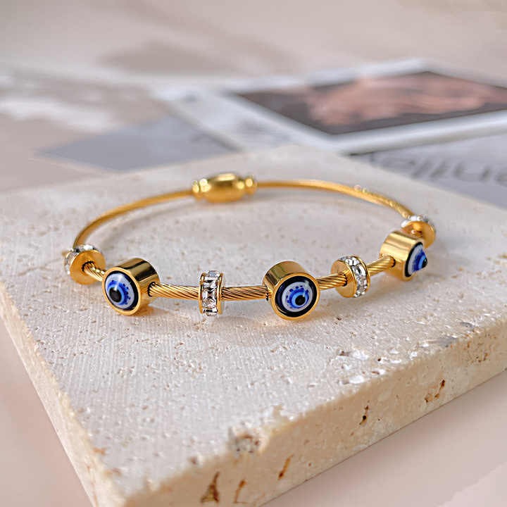 Devil’s eye gold wire bracelet with alternating crystal and evil eye beads displayed on textured stone.