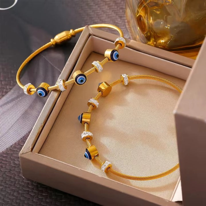 Boxed set of two golden evil eye bangles, showcasing crystal and enamel bead details.
