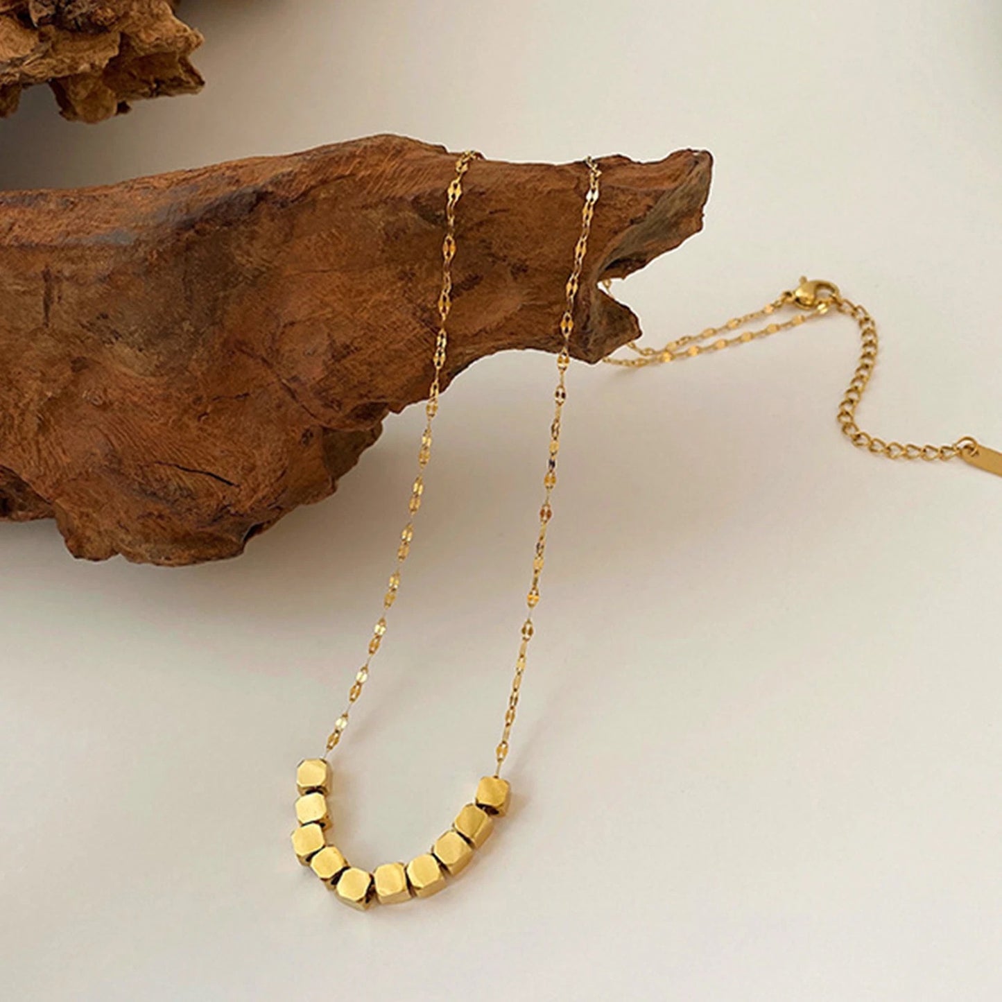 Geometric gold bead necklace displayed on wooden prop