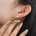 Model wearing one bold hammered gold V earring while gently touching her ear, emphasizing its size and statement presence