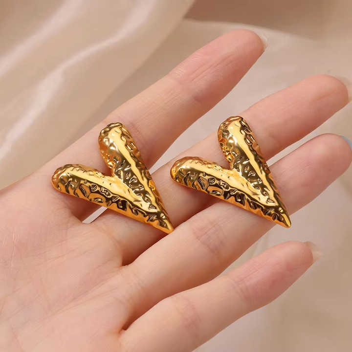 Textured gold V earrings resting on a model’s hand, capturing their size, finish, and bold design against a satin background