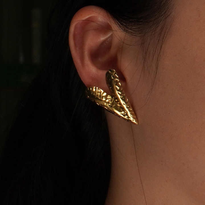 Close-up of a model wearing one V-shaped textured gold earring, highlighting its fit and sculptural design against her skin.