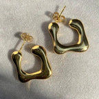 Top view of irregular C gold studs on textured surface with natural lighting.