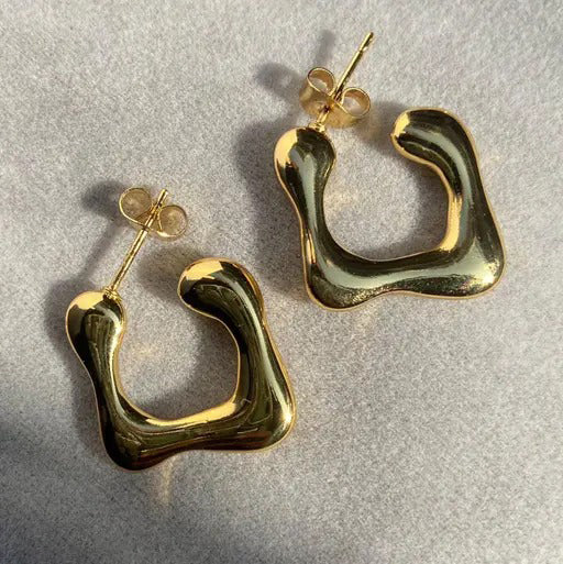 Top view of irregular C gold studs on textured surface with natural lighting.