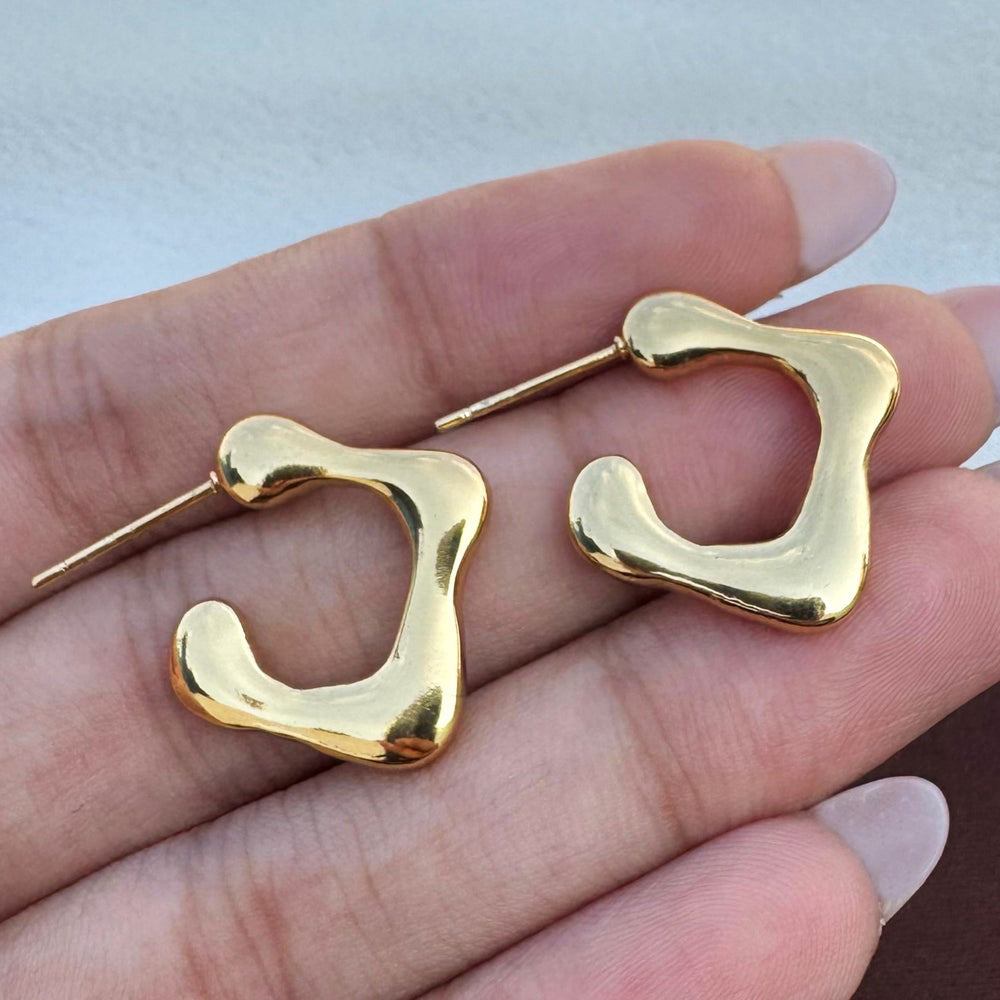 Close-up of hand holding the earrings, showing their unique shape and shiny finish.