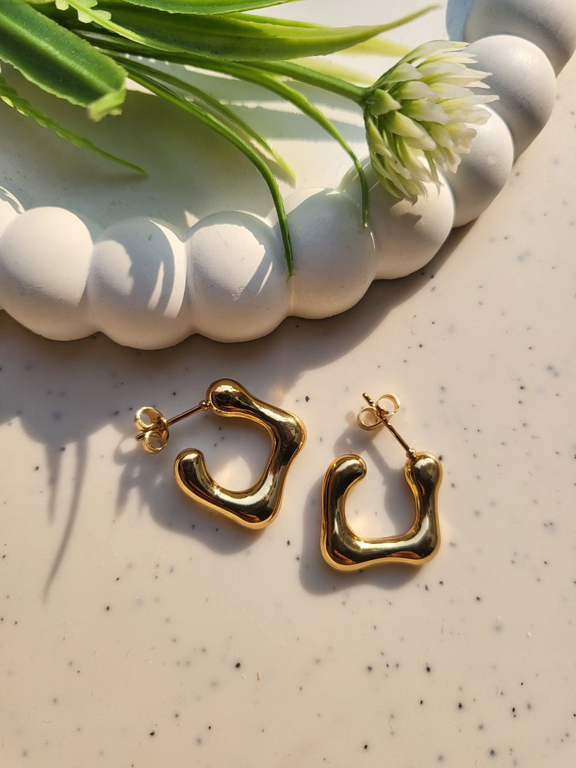 Irregular C earrings styled with artificial flower and ceramic decor in bright sunlight.