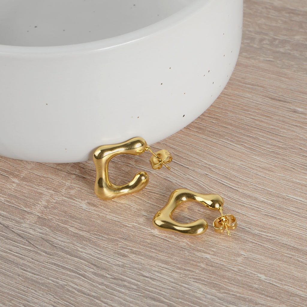 Close-up of C-shaped abstract earrings beside a white bowl on a wooden surface.