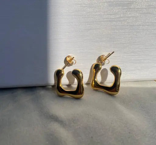 Pair of glossy gold irregular C-shaped earrings placed against a white backdrop and soft shadow.