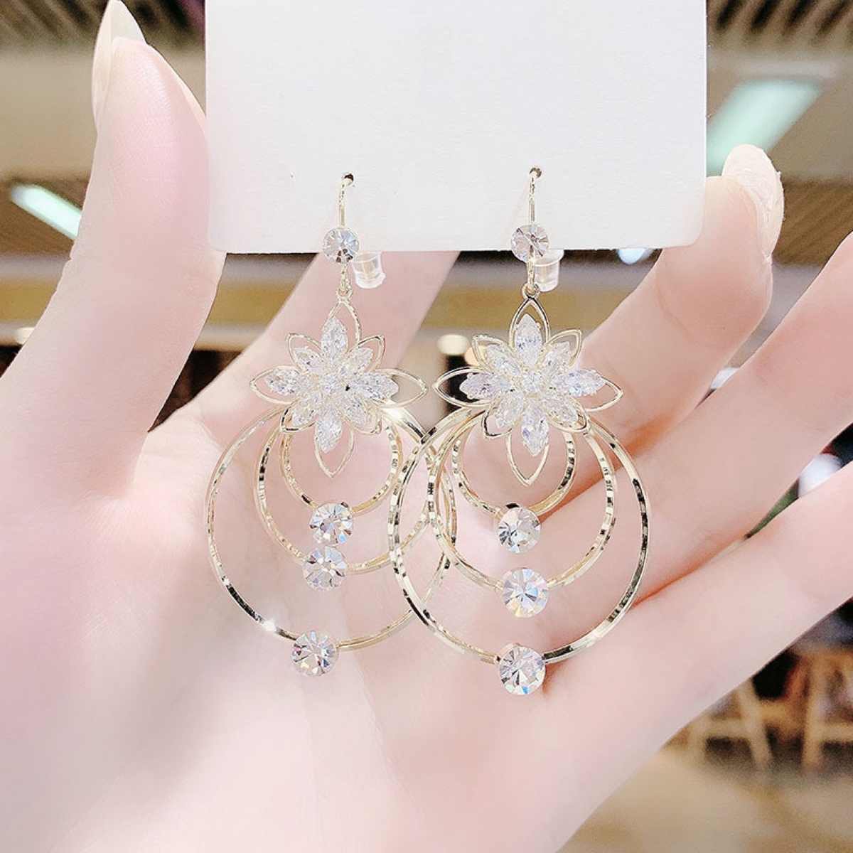 Gold floral earrings held in a hand with a blurred indoor background