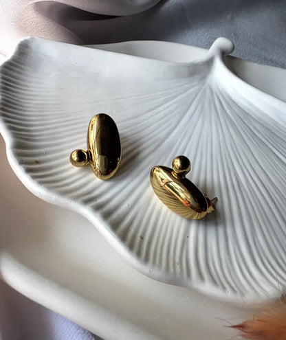 Close-up of Pebble Earrings on a white ceramic leaf plate, showcasing their glossy gold finish