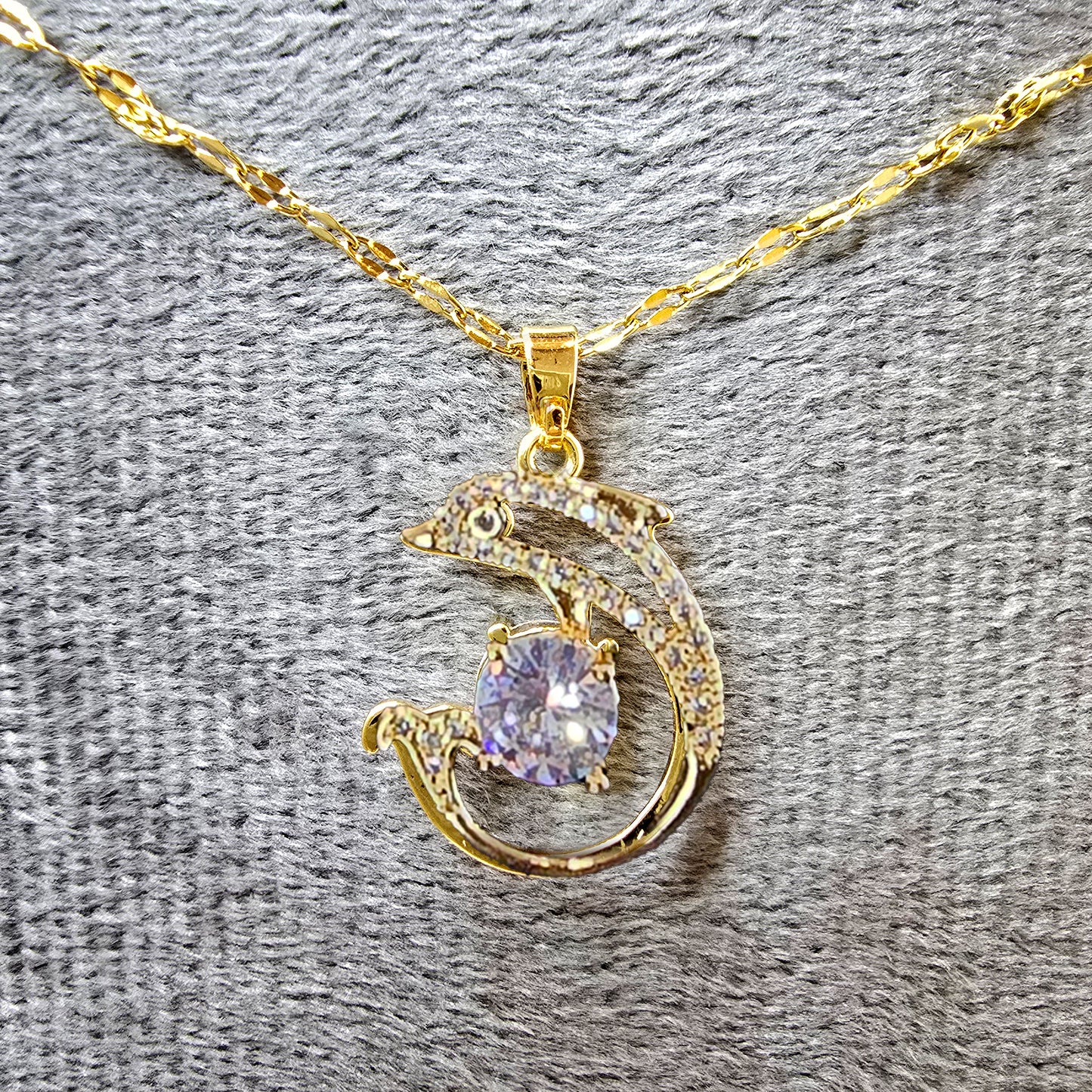 Gold Dolphin Pendant Necklace on grey velvet background highlighting sparkle.
