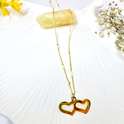 Necklace on shell background featuring minimalist gold twin heart design.