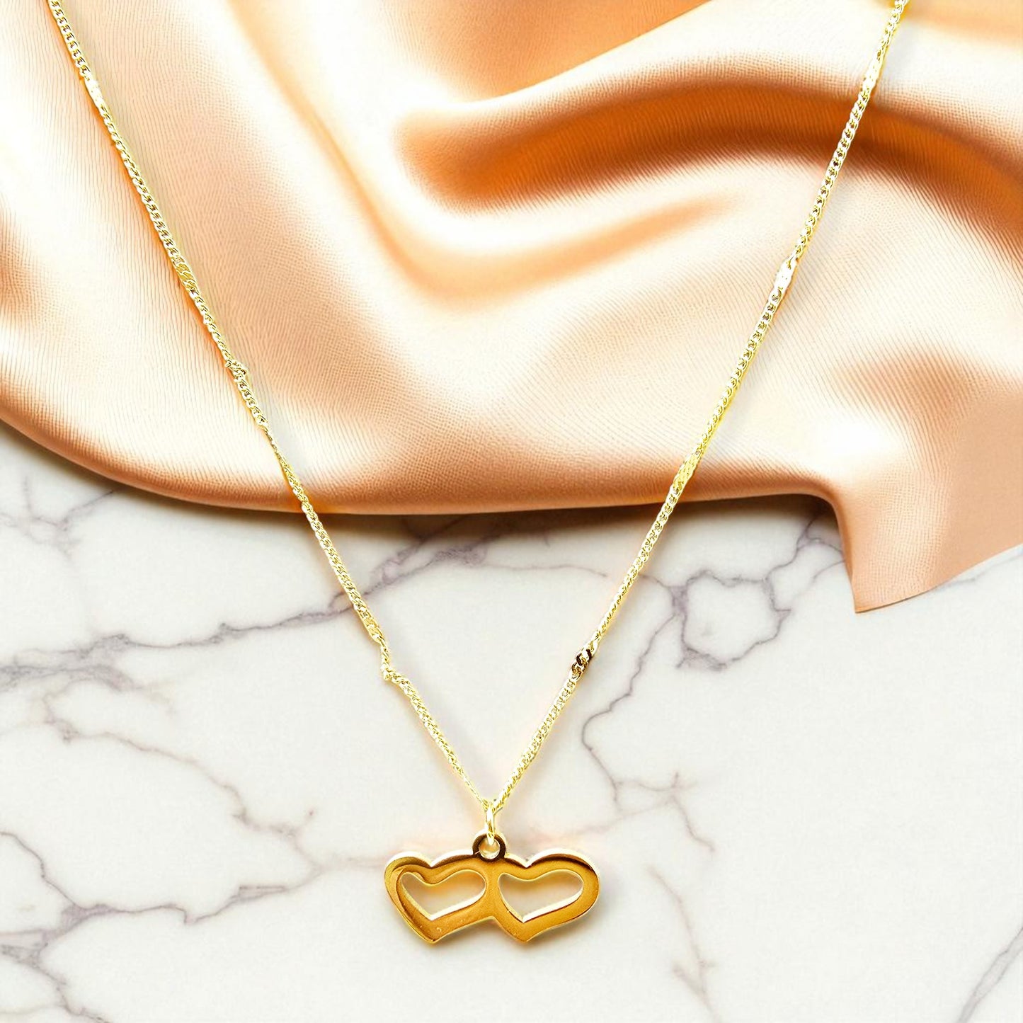 Close-up of Twin Heart Necklace on satin and marble surface highlighting reflective shine.