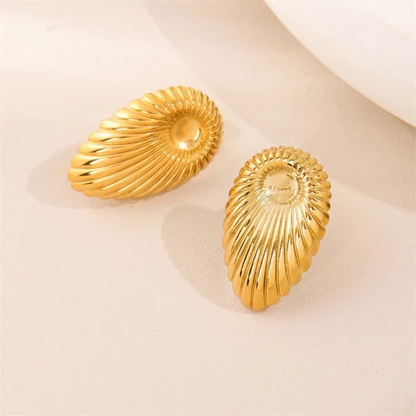 Golden shell earrings captured under natural light, placed on a pastel surface to highlight their rich texture and polished finish