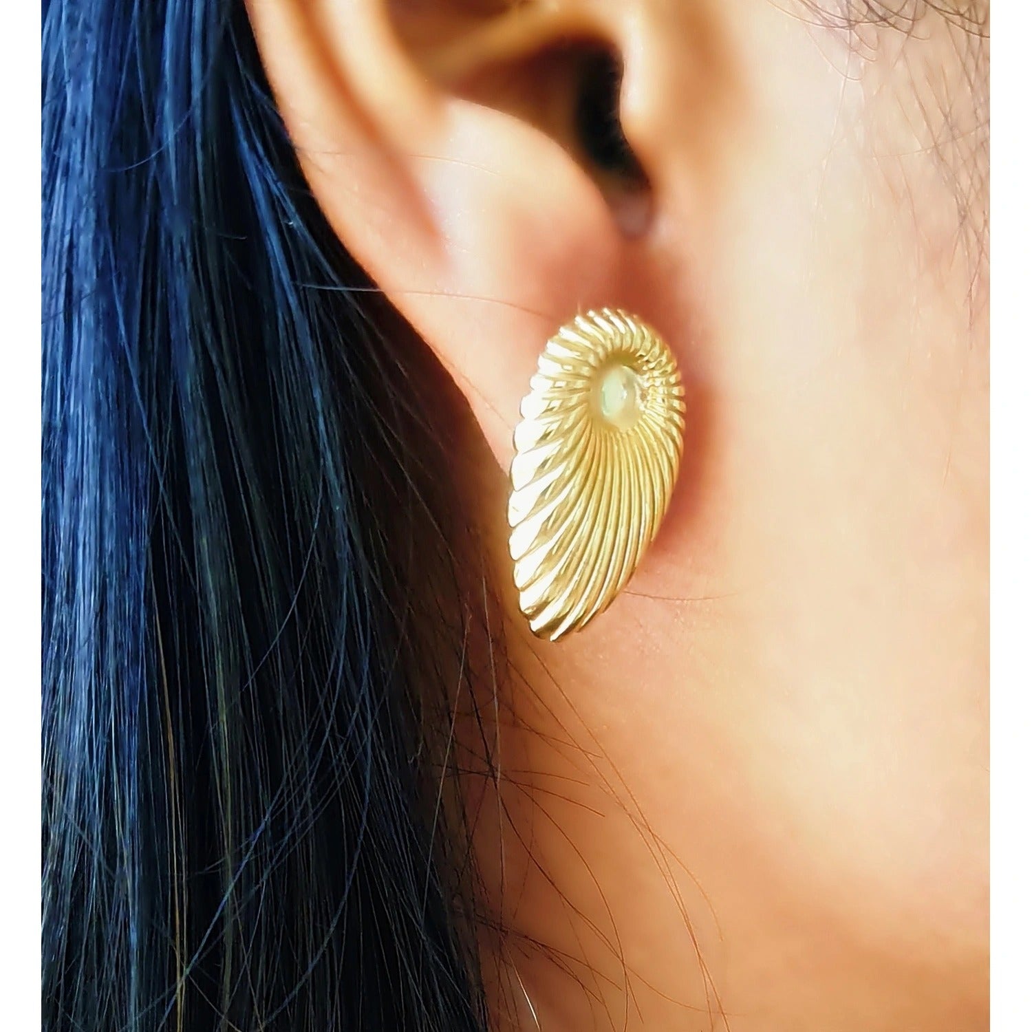 Close-up of a woman wearing a single golden shell earring, showing the elegant fit and size on the earlobe against dark hair