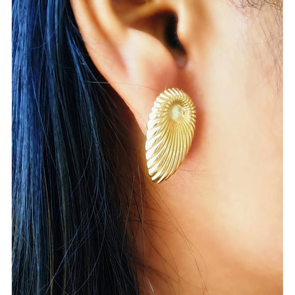Close-up of a woman wearing a single golden shell earring, showing the elegant fit and size on the earlobe against dark hair
