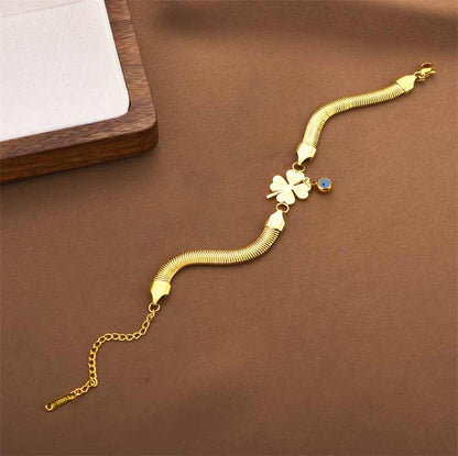 Flatlay of gold snake chain bracelet featuring four-leaf clover and evil eye