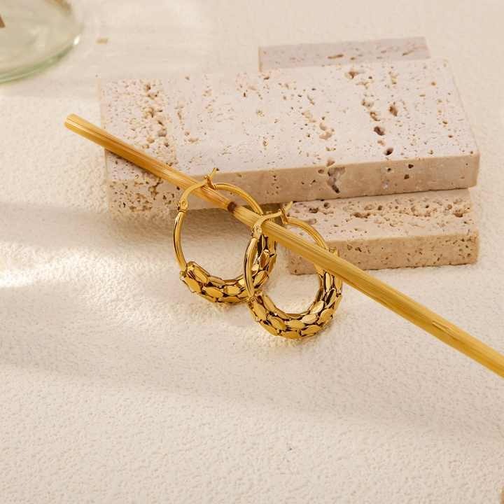 Gold hoop earrings on a textured surface with a neutral background