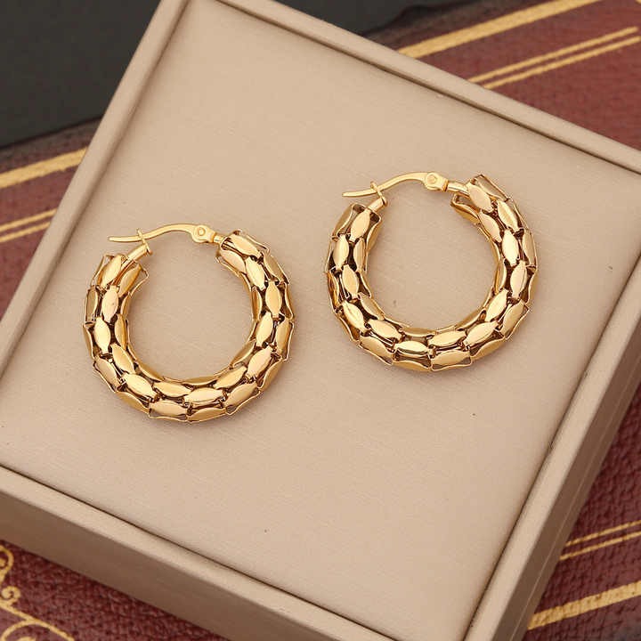 Gold hoop earrings on a beige jewelry box with a patterned fabric background