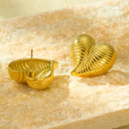 Back view of striped heart earrings showing the gold pin post, displayed on textured beige stone
